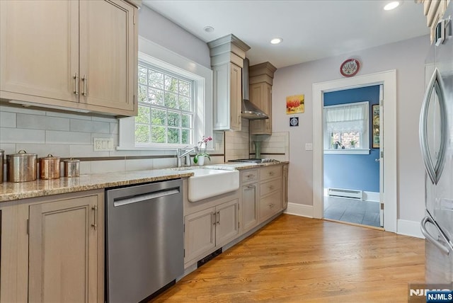 kitchen featuring wall chimney range hood, appliances with stainless steel finishes, baseboard heating, a sink, and tasteful backsplash