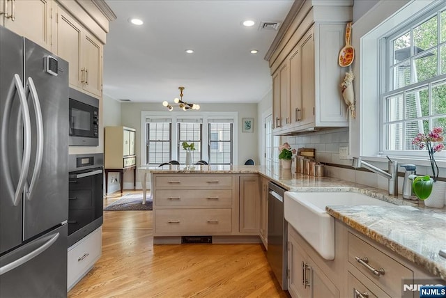 kitchen featuring appliances with stainless steel finishes, an inviting chandelier, light wood finished floors, a peninsula, and recessed lighting