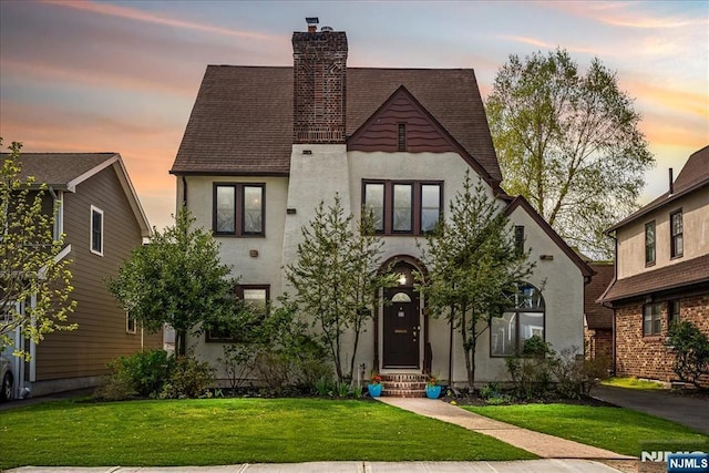 view of front of home featuring stucco siding, a chimney, a shingled roof, entry steps, and a lawn