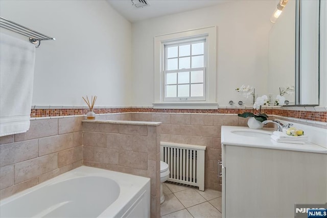 bathroom featuring vanity, toilet, tile patterned floors, radiator, and a garden tub