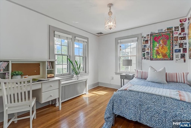 bedroom with visible vents, an inviting chandelier, wood finished floors, baseboards, and radiator heating unit