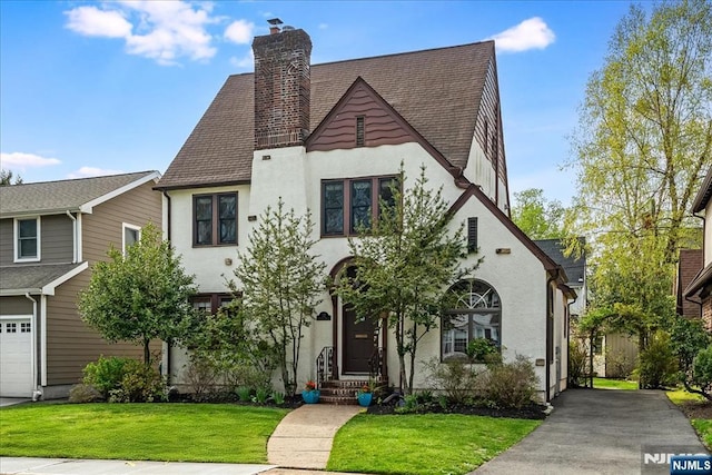 tudor-style house with stucco siding, a front yard, and a chimney