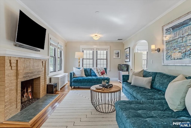 living room featuring a brick fireplace, arched walkways, wood finished floors, visible vents, and ornamental molding
