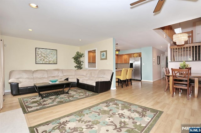 living area with baseboards, recessed lighting, ceiling fan with notable chandelier, and light wood-style flooring