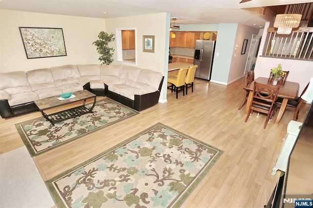 living room with baseboards, ceiling fan with notable chandelier, and light wood-style flooring