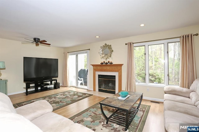 living room featuring a fireplace with flush hearth, ceiling fan, visible vents, baseboards, and wood finished floors