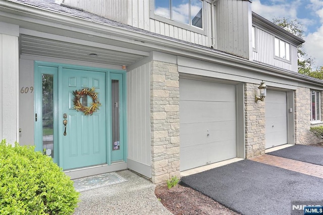 doorway to property with a garage, board and batten siding, driveway, and stone siding