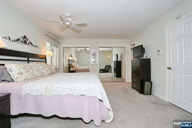 bedroom featuring a ceiling fan, light colored carpet, and two closets