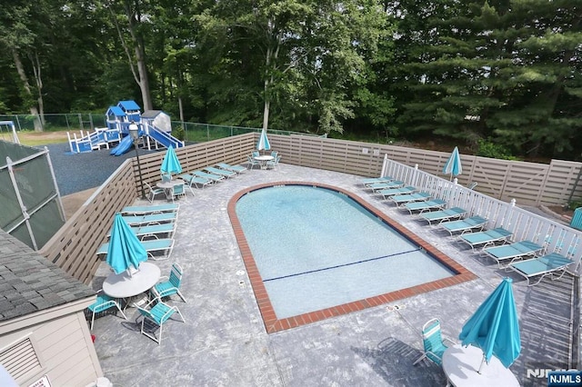 pool featuring fence, playground community, and a patio area
