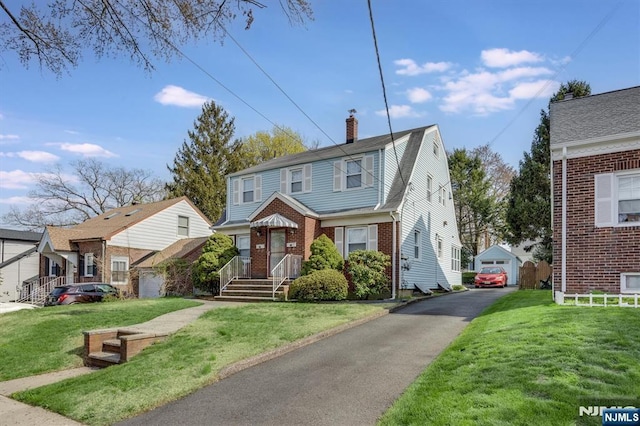 view of front of property with a chimney, brick siding, an outbuilding, a detached garage, and a front lawn