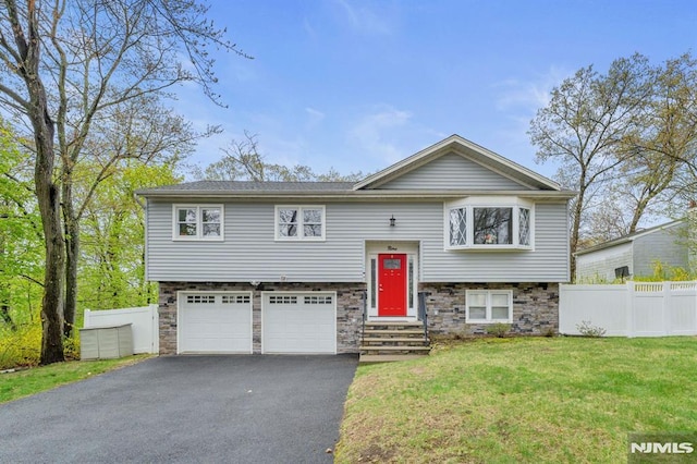 raised ranch featuring fence, aphalt driveway, a garage, stone siding, and a front lawn