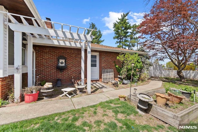 rear view of house featuring brick siding, fence, a patio area, a vegetable garden, and a pergola