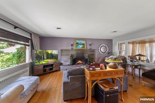 living area featuring wood finished floors, visible vents, and a warm lit fireplace