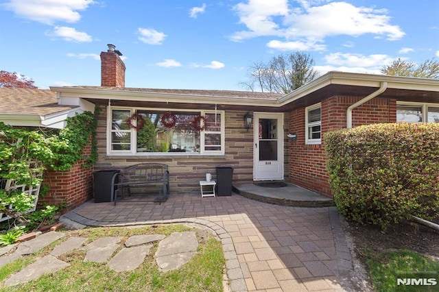back of property featuring a chimney, a patio area, and brick siding