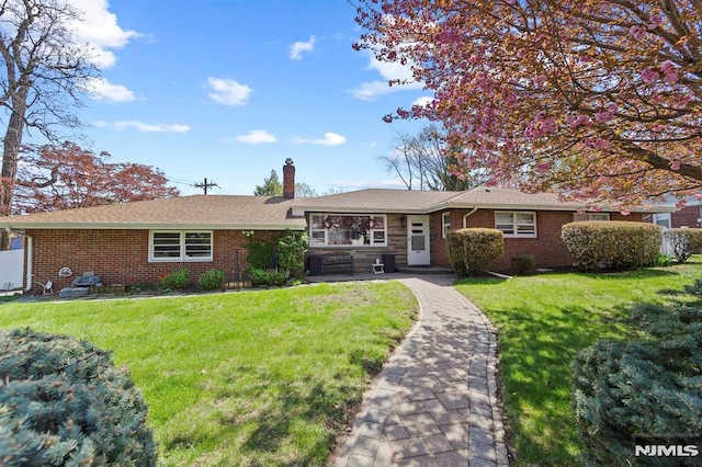 ranch-style home with a chimney, brick siding, and a front yard