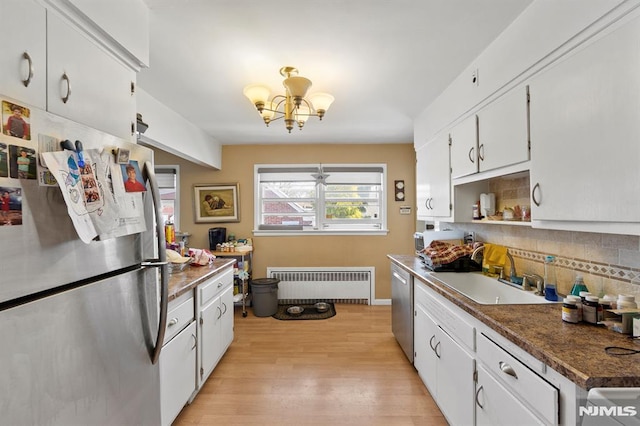 kitchen featuring a sink, appliances with stainless steel finishes, light wood-type flooring, radiator heating unit, and backsplash