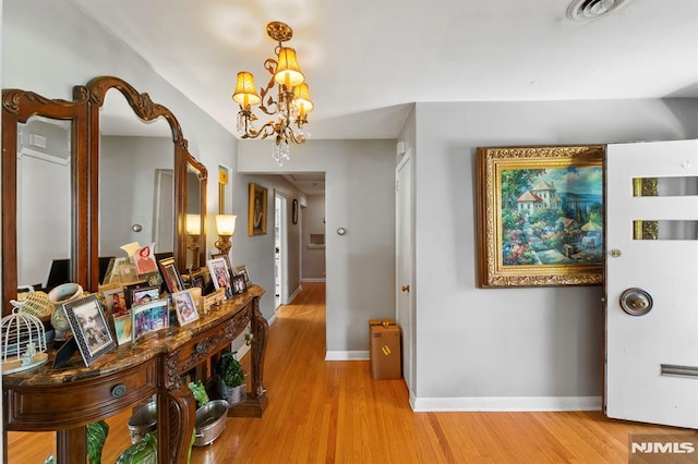 hall with baseboards, visible vents, a notable chandelier, and light wood-style floors