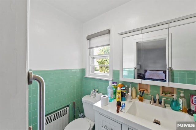 bathroom featuring radiator, toilet, tile walls, vanity, and wainscoting