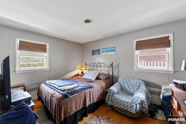 bedroom featuring wood finished floors, visible vents, and radiator