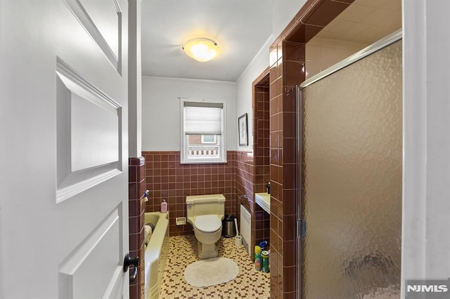 full bath featuring toilet, a shower stall, a wainscoted wall, and tile walls