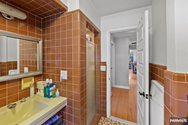 bathroom with a sink, a stall shower, and tile walls