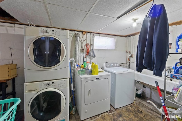clothes washing area with concrete block wall, stacked washer / drying machine, separate washer and dryer, and laundry area