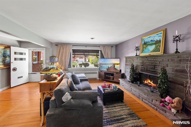 living room with light wood-type flooring, a stone fireplace, and radiator