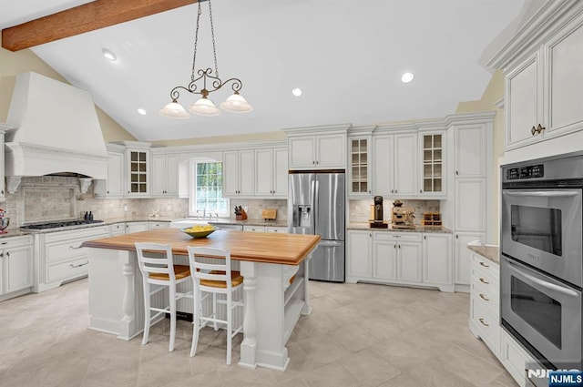 kitchen with wood counters, stainless steel appliances, decorative backsplash, premium range hood, and white cabinets