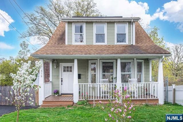 bungalow-style home with a front yard, roof with shingles, covered porch, and fence