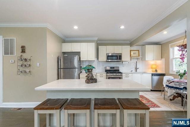 kitchen featuring white cabinets, stainless steel appliances, ornamental molding, and a kitchen bar