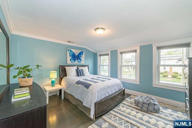 bedroom with baseboards, ornamental molding, wood finished floors, and multiple windows