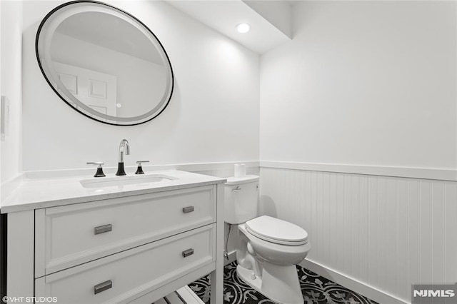 half bathroom featuring vanity, toilet, a wainscoted wall, and recessed lighting