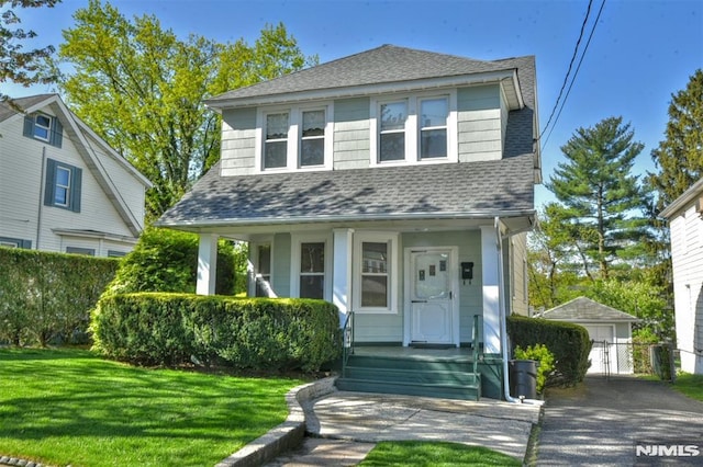traditional style home featuring a porch, roof with shingles, a front yard, and a detached garage