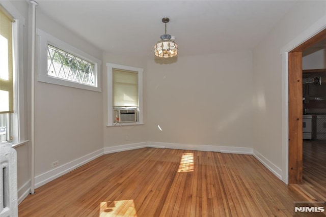 unfurnished dining area featuring an inviting chandelier, light wood-style flooring, baseboards, and cooling unit