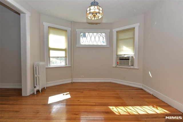 unfurnished dining area featuring baseboards, light wood-style flooring, radiator, and a chandelier