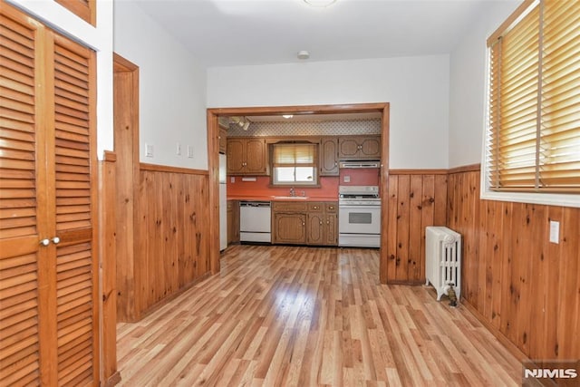 kitchen featuring radiator, wood walls, wainscoting, and white appliances