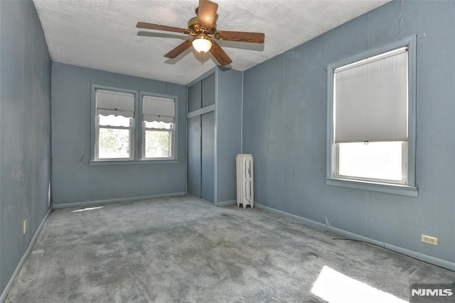 unfurnished room featuring carpet flooring, ceiling fan, and radiator heating unit