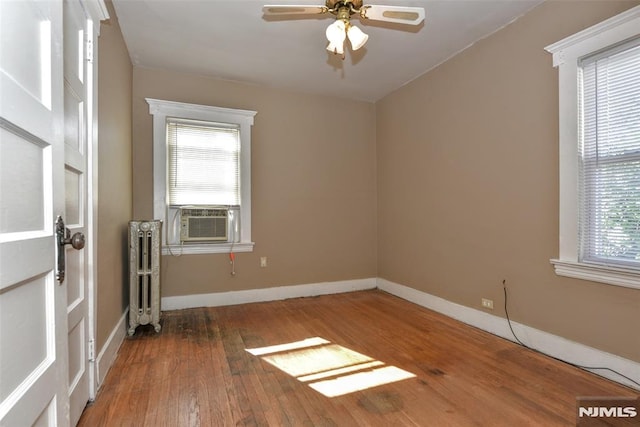 unfurnished room with hardwood / wood-style floors, baseboards, ceiling fan, radiator heating unit, and cooling unit