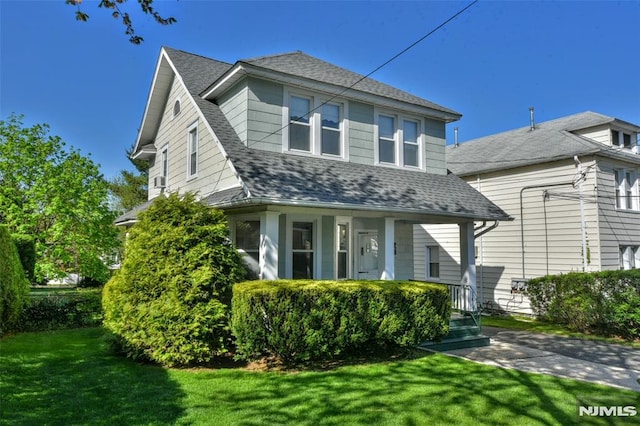 view of front of property featuring roof with shingles, covered porch, and a front yard