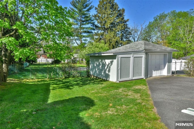view of outdoor structure with fence, an outbuilding, and driveway