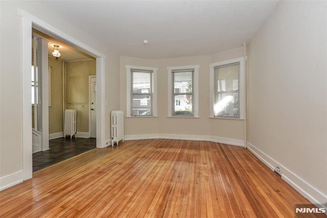 unfurnished room featuring baseboards, an inviting chandelier, light wood-style flooring, and radiator