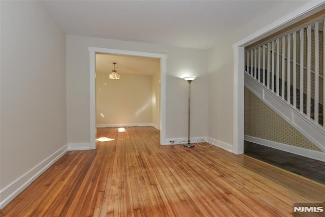 empty room featuring baseboards, a notable chandelier, and hardwood / wood-style floors