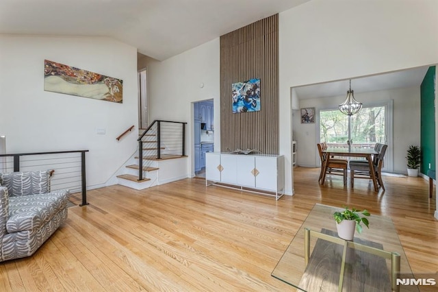 living area with a notable chandelier, high vaulted ceiling, baseboards, wood finished floors, and stairway