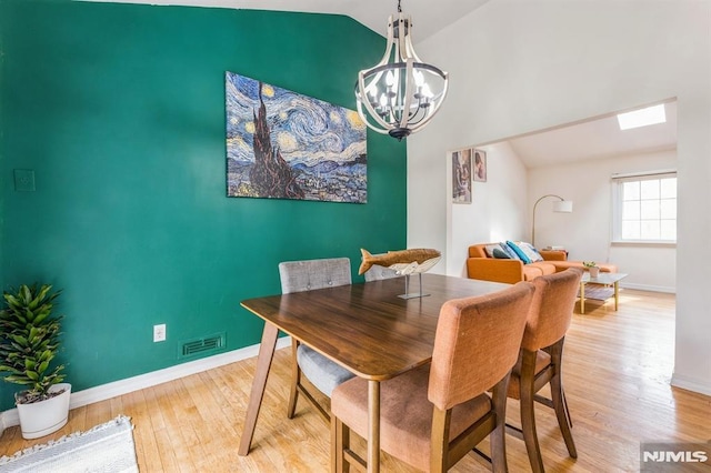 dining room with a notable chandelier, lofted ceiling, wood finished floors, and visible vents