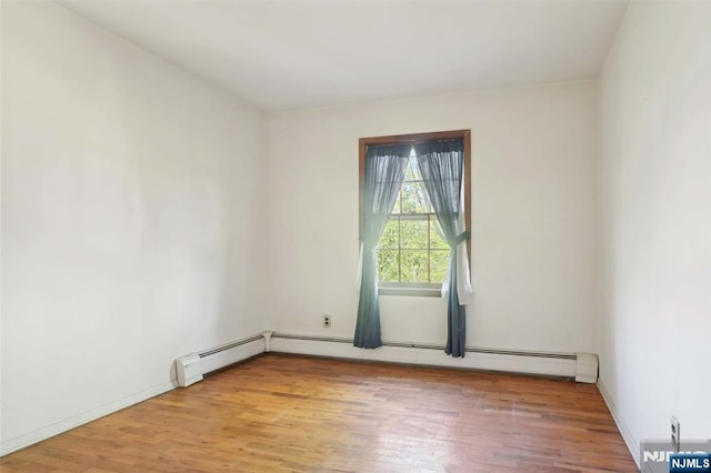 spare room featuring baseboards, light wood-style flooring, and a baseboard heating unit