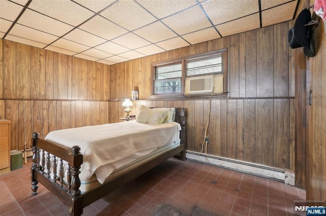 bedroom with a paneled ceiling, a baseboard heating unit, and wooden walls