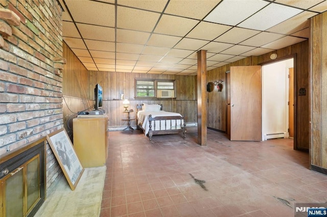 bedroom featuring a drop ceiling, a fireplace, a baseboard heating unit, and wood walls