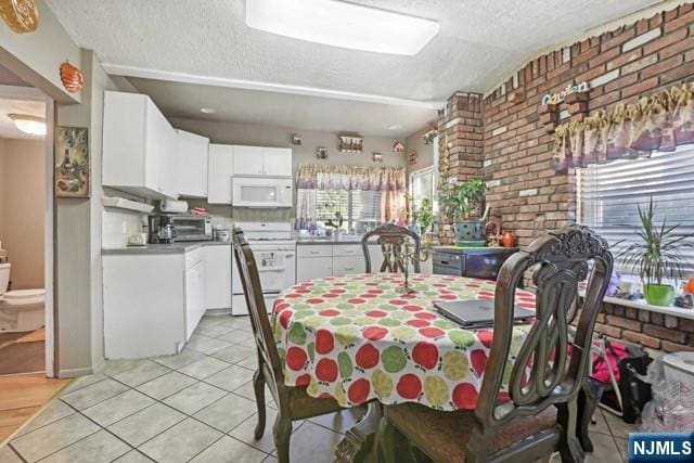 dining area with light tile patterned flooring, a textured ceiling, brick wall, and a healthy amount of sunlight