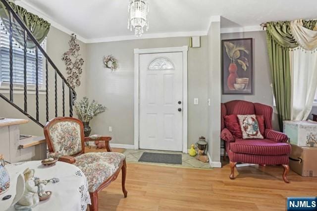 entryway featuring crown molding, an inviting chandelier, wood finished floors, baseboards, and stairway