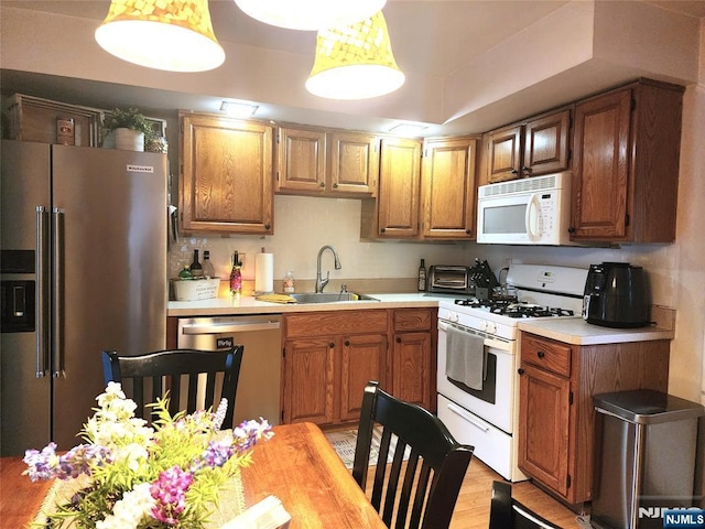 kitchen with appliances with stainless steel finishes, a sink, light countertops, light wood-style flooring, and brown cabinetry